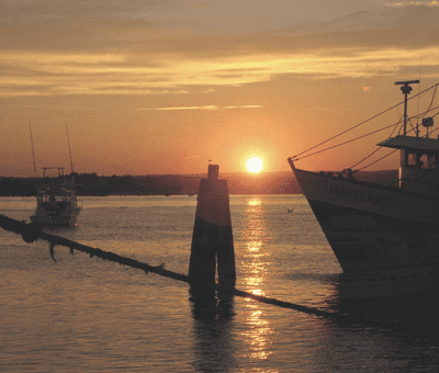 A boat docked in the water at sunset.