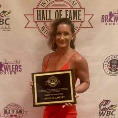 A woman in a red dress holding an award for the hall of fame.