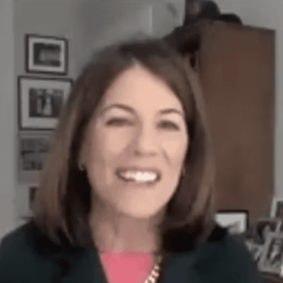 A woman in a suit is smiling in front of a desk.