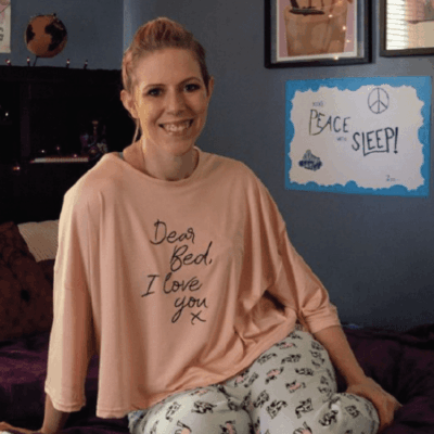 A woman in pajamas sitting on a bed with a sign.