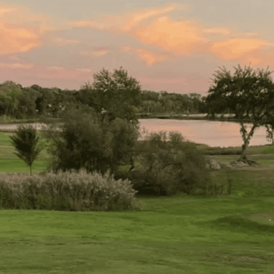 A golf course with trees and a lake at sunset.
