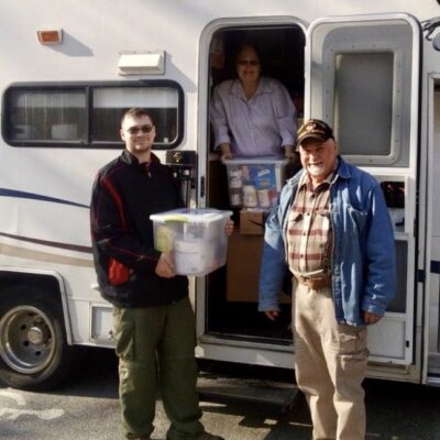 Two men standing in front of a rv with boxes.