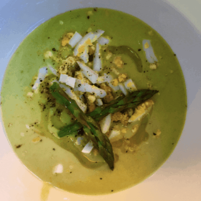 A bowl of green soup with asparagus and eggs.