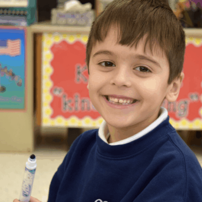 A young boy smiling while holding a pen.