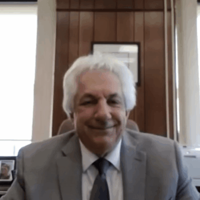 A man in a suit and tie sitting in front of an american flag.