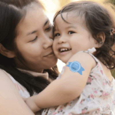 A woman holding a child with a blue sticker on her arm.