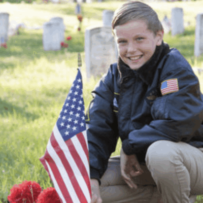 A boy kneeling in front of a grave with an american flag.
