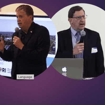 Two men are speaking in front of a purple background.