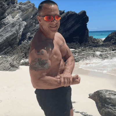 A man standing on a beach with a shirt and sunglasses.