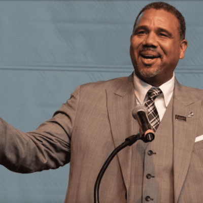 A man in a suit and tie is speaking into a microphone.