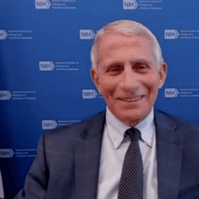 A man in a suit and tie sitting in front of an american flag.