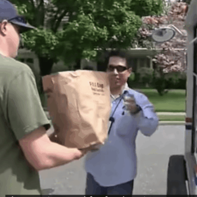 A man is handing a bag to a man in front of a delivery truck.