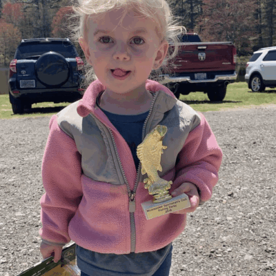 A little girl holding a trophy in a parking lot.