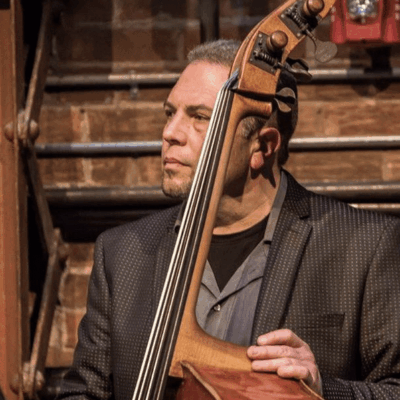 A man playing a double bass in front of a brick wall.