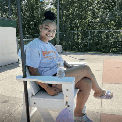 A young woman sitting in a white chair with an umbrella.