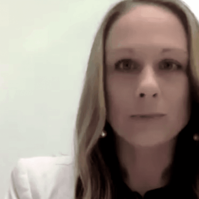 A woman in a white blazer is looking at the camera.