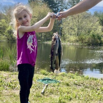 A little girl holds up a fish in front of a man.