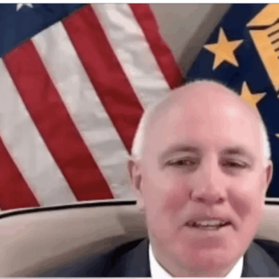 A man in a suit and tie is sitting in front of an american flag.