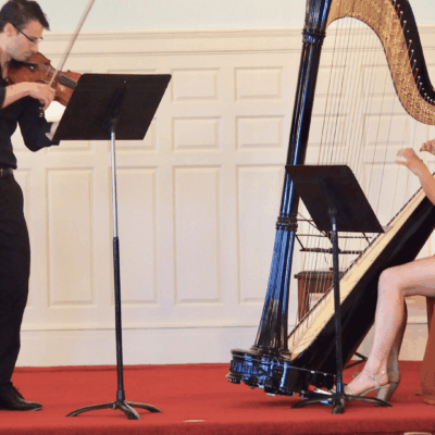 Two people playing a harp in front of an audience.