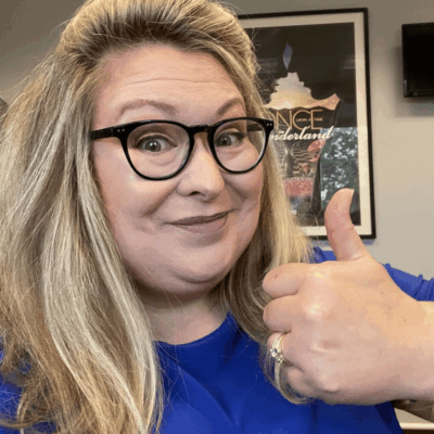 A woman in glasses giving a thumbs up.