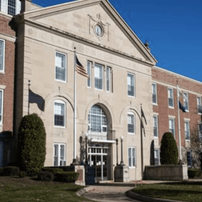 The front of a brick building with trees and bushes.