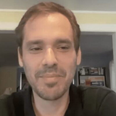 A man in a black shirt is smiling in front of a camera.