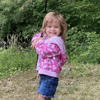 A little girl holding a fishing pole in the grass.