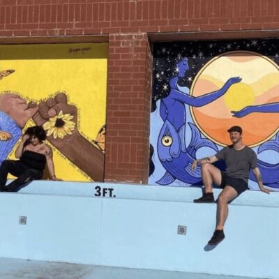 Two people sitting on a wall next to a mural.