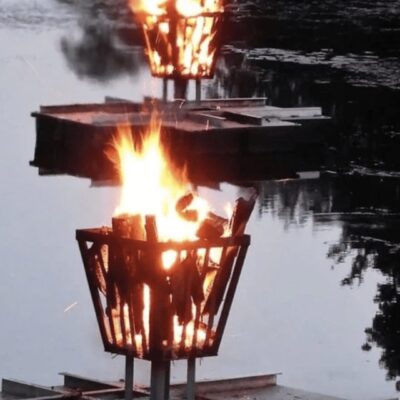 Two baskets with fire on top of a body of water.