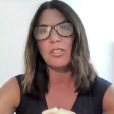 A woman in glasses is holding a microphone.