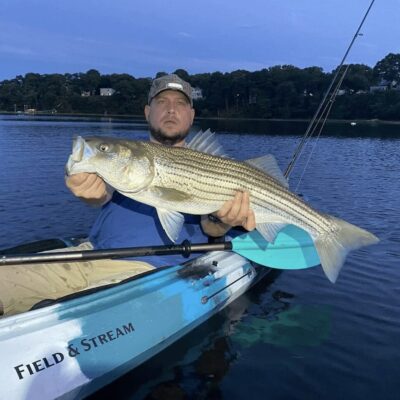 A man in a kayak holding a striped bass.