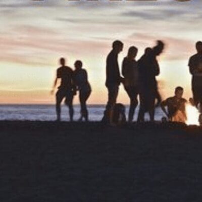 A group of people standing around a campfire at sunset.