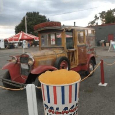 A vintage car with a bucket of popcorn in front of it.