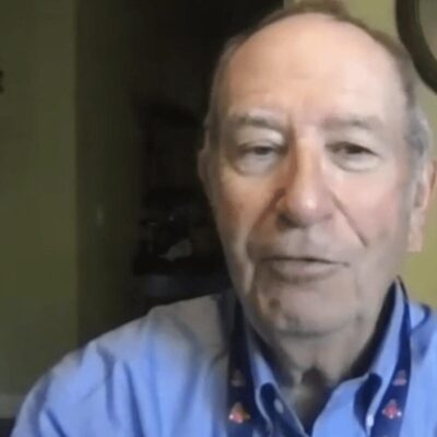 A man in a blue shirt is talking to a camera.