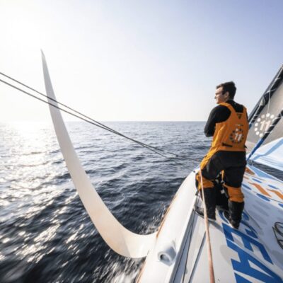 A man is standing on the bow of a sailboat.
