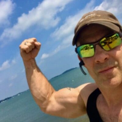 A man flexing his biceps in front of a body of water.