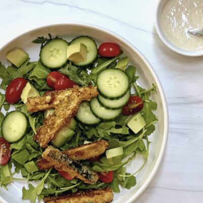 A salad with fried sardines, tomatoes and cucumbers.