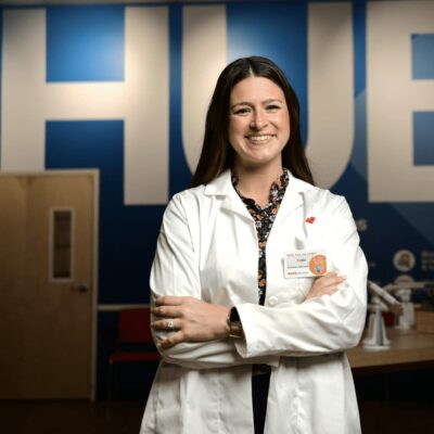 A woman in a lab coat standing in front of a blue wall.