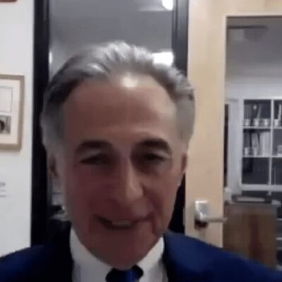 A man in a suit and tie is talking on a video.