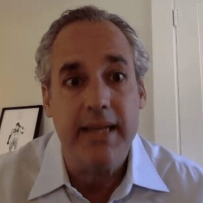 A man in a blue shirt is talking to a camera.