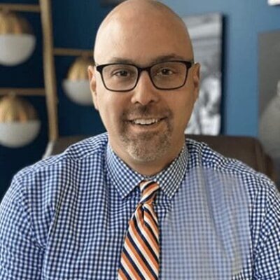A bald man wearing glasses and a blue and orange tie.
