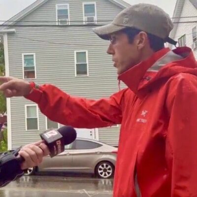 A man in a red jacket is talking to a reporter in a raincoat.