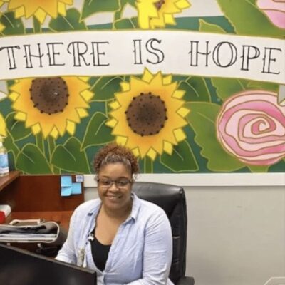 A woman sitting in front of a desk with sunflowers on the wall.