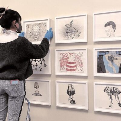 A woman looking at framed drawings on a wall.