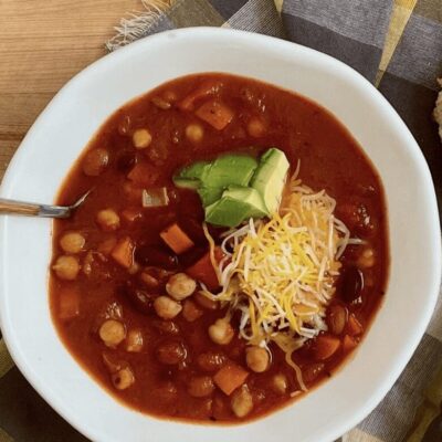 A bowl of chili with bread and avocado.