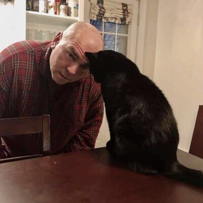 A man petting a black cat at a table.
