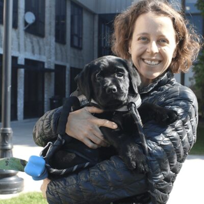 A woman holding a black labrador puppy.
