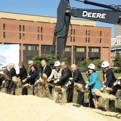 A group of people standing in front of an excavator.