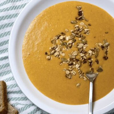 A bowl of pumpkin soup with granola and bread.