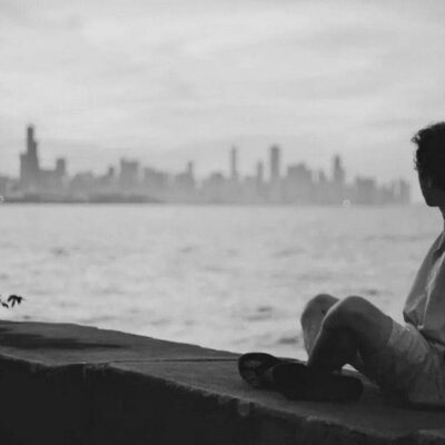 A man sits on a ledge looking out over the water.